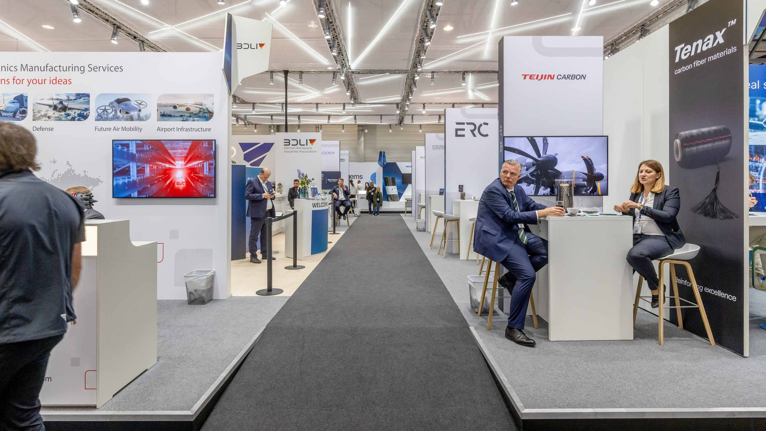Kleine Reihenstände säumen beidseitig einen Gang in Halle A, vorn der Teijin-Carbon-Stand.