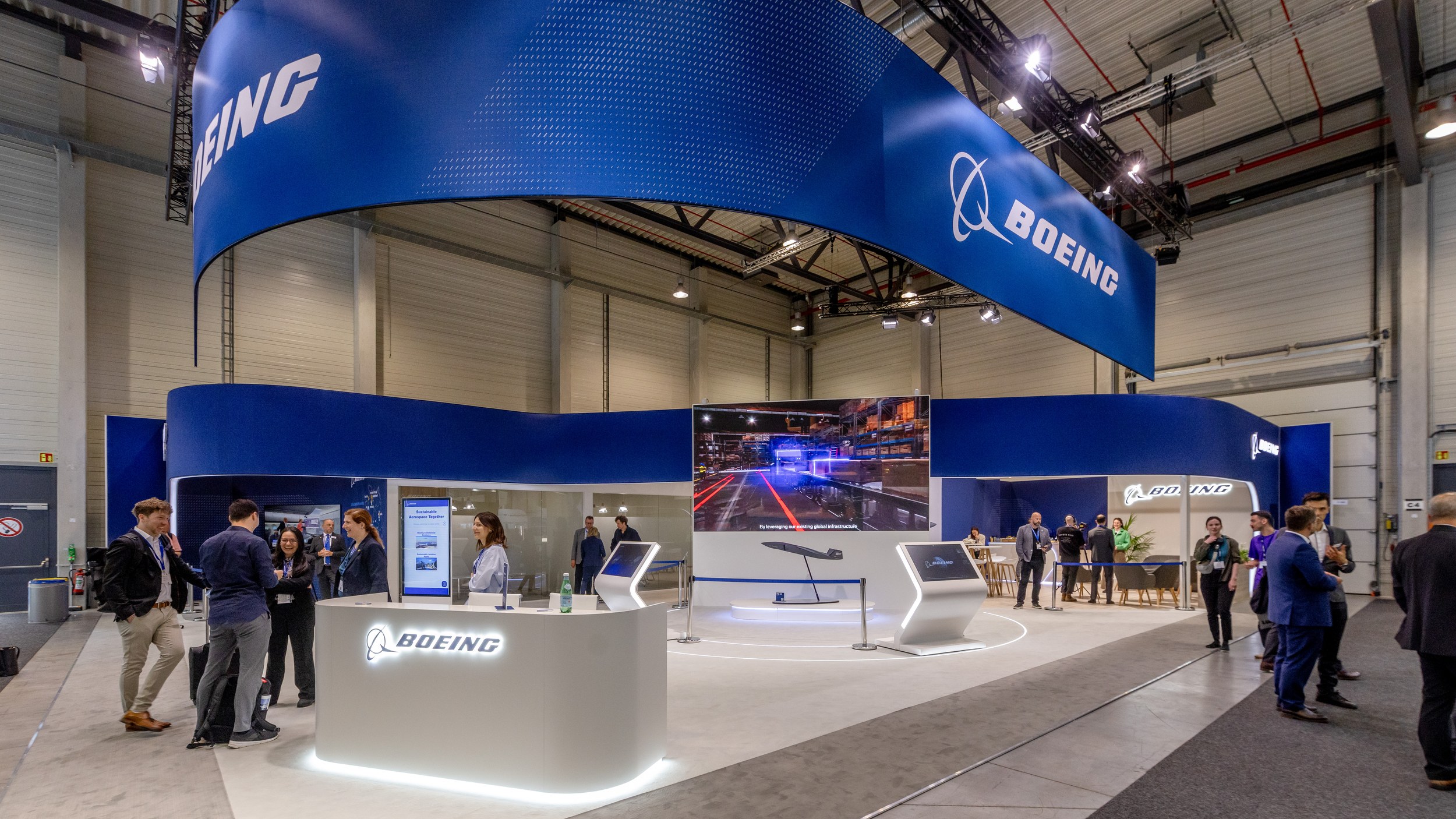 Weitwinkelblick auf den Boeing-Stand in Halle C mit großem blauen Deckenbanner und beleuchteter Empfangstheke.