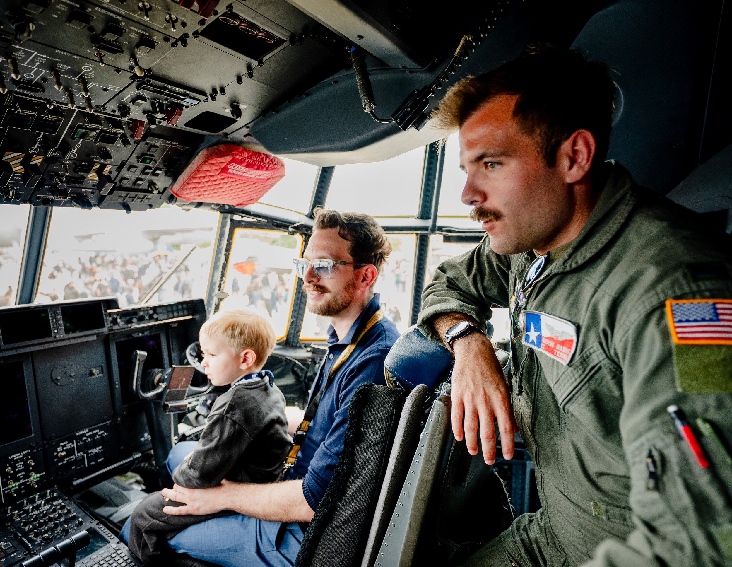 Ein Crewmitglied im grünen Fluganzug lehnt sich im Cockpit einer Lockheed Martin C-130 Hercules neben einen erwachsenen …