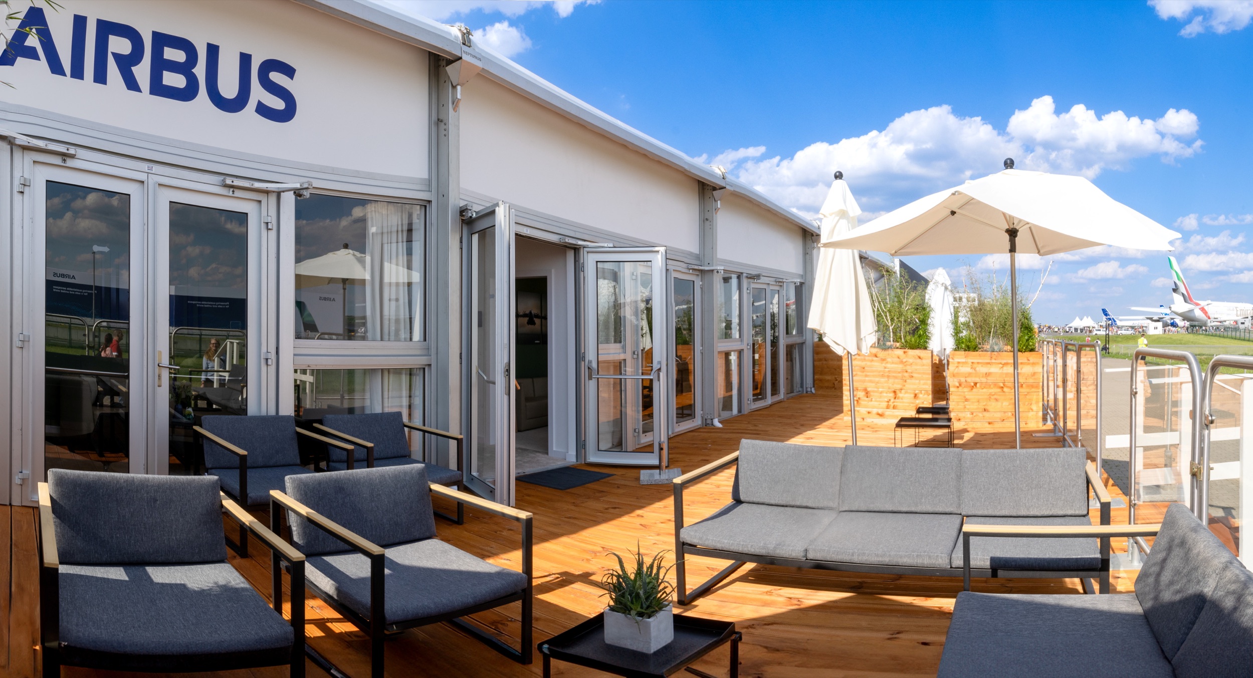 Terrasse des Airbus-Chalets der ILA 2024 mit Lounge-Möbeln, Sonnenschirmen und Blick auf das Static Display.